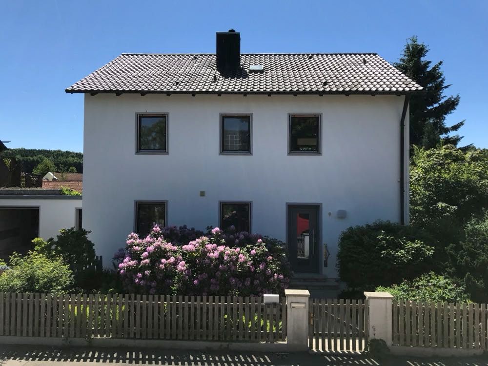 Freistehendes weißes Wohnhaus mit Satteldach, Vorgarten mit blühendem Rhododendron und Holzzaun