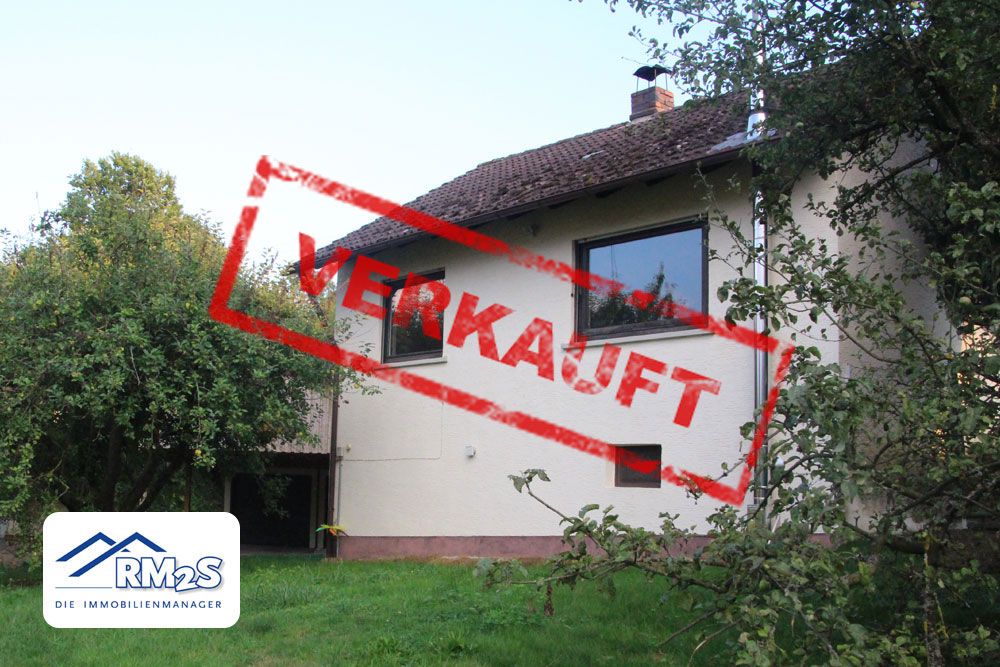 Wohnhaus mit Satteldach, umgeben von Bäumen und Wiese